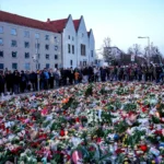 Люди возлагают цветы и зажигают свечи перед церковью Святого Иоанна