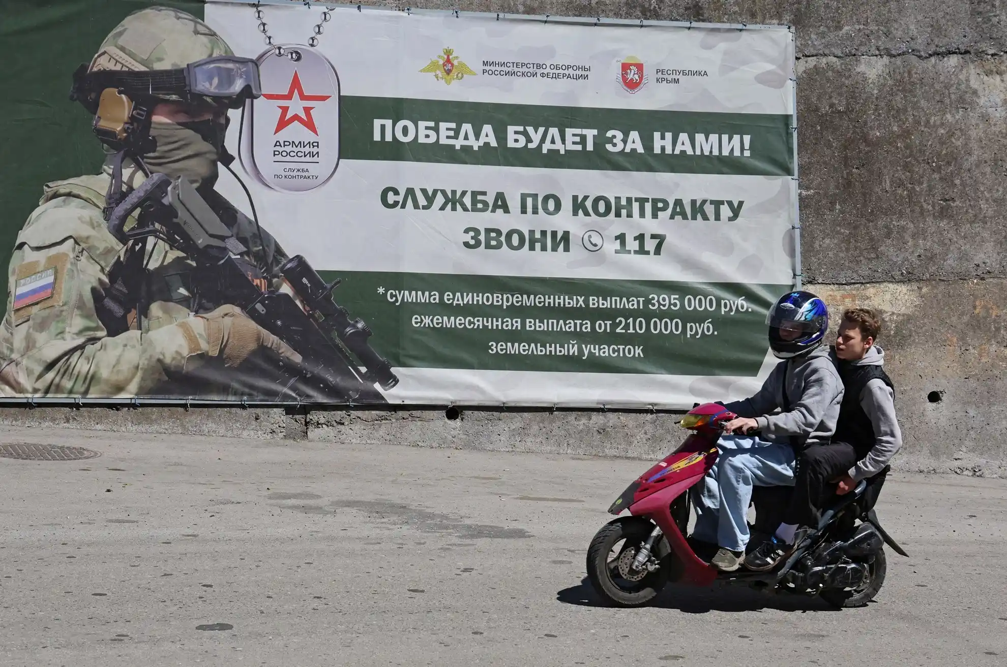 Люди едут на мопеде мимо баннера