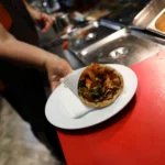 A cook holds a plate of souvlaki