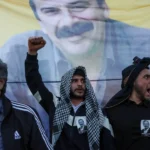 Люди выкрикивают лозунги перед портретом Сирри Сурейи Ондера